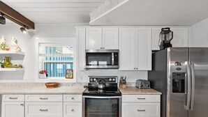 A modern kitchen with white cabinetry, stainless steel appliances, and a window with a view of a blue building.
