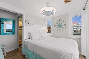A bedroom with a large bed, a wall-mounted compass, and a window with blinds. - South Wind: Gorgeous Beachfront Home, Private Pool, Hot Tub, Fire Pit (St. George Island)