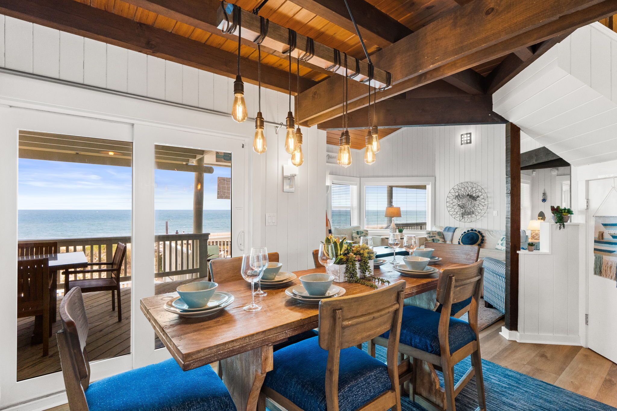 A dining area with a wooden table and chairs, a view of the ocean, and pendant lighting.