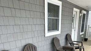 A row of Adirondack chairs against a grey shingle wall with a window and a door.