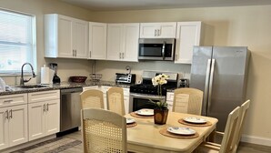 A modern kitchen with white cabinets, stainless steel appliances, and a dining area with wooden chairs and a table.