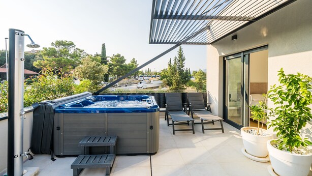 A modern outdoor patio with a hot tub, seating area, and potted plants.