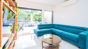 A modern living room with a teal sectional sofa, a glass coffee table, and a view of the outdoors through large windows.