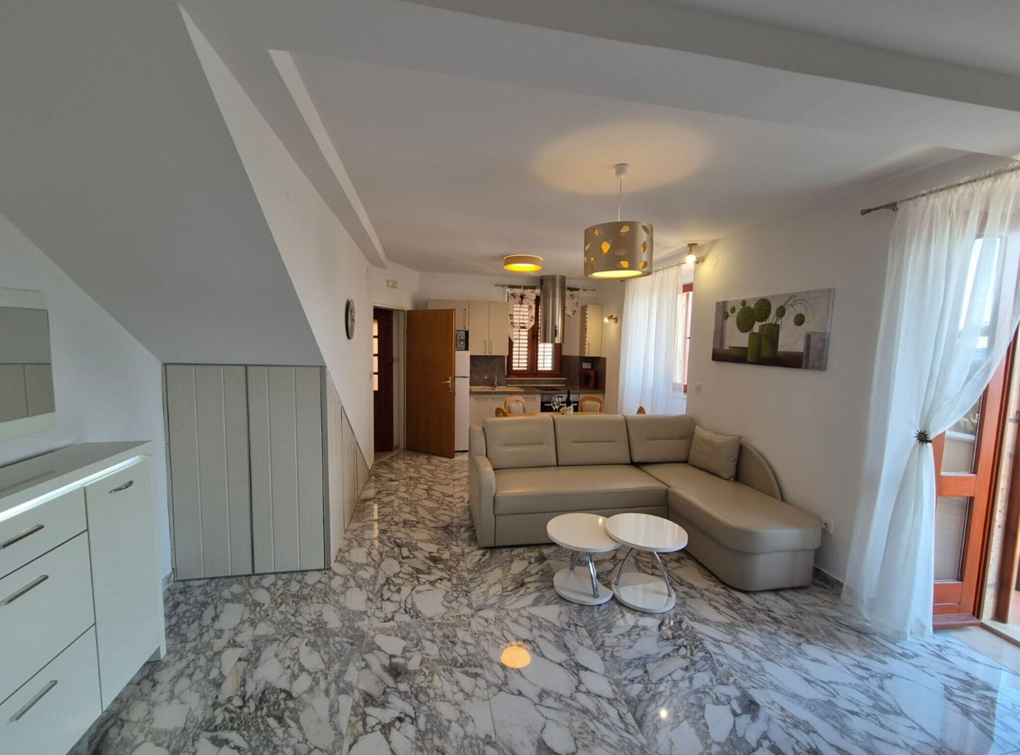 Un salon moderne avec un sol en marbre, un canapé d’angle beige et un coin repas comprenant une petite table et des chaises.