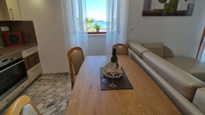 A dining area with a wooden table, chairs, a sofa, and a view of the sea through a window. - Villa Ana Apartments - One Bedroom Apartment with Terrace and Sea View (Mlini)