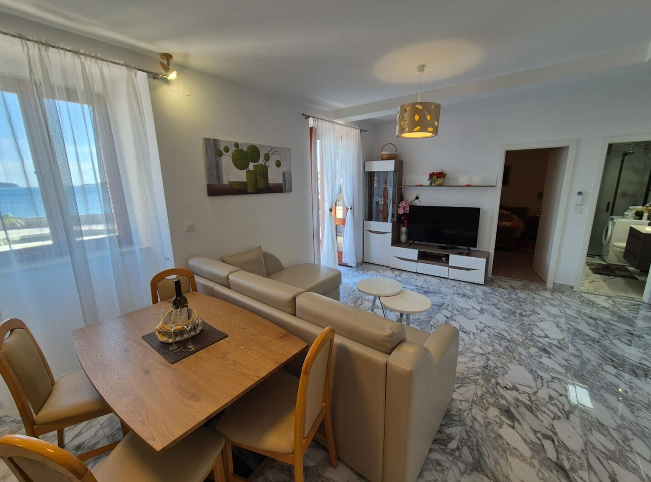 Een moderne woonkamer met een houten eettafel, beige banken, een televisie en een marmeren vloer.