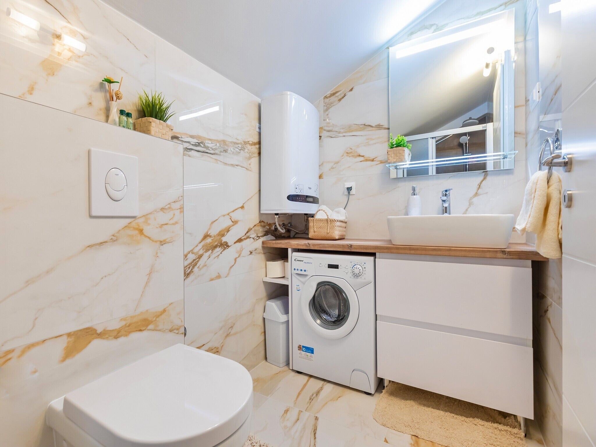 Une salle de bain moderne avec un pare-feu en marbre, un lave-linge encastré, un lavabo et des toilettes.