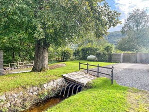 A rustic bridge over a stream, surrounded by lush greenery and a wooden fence.