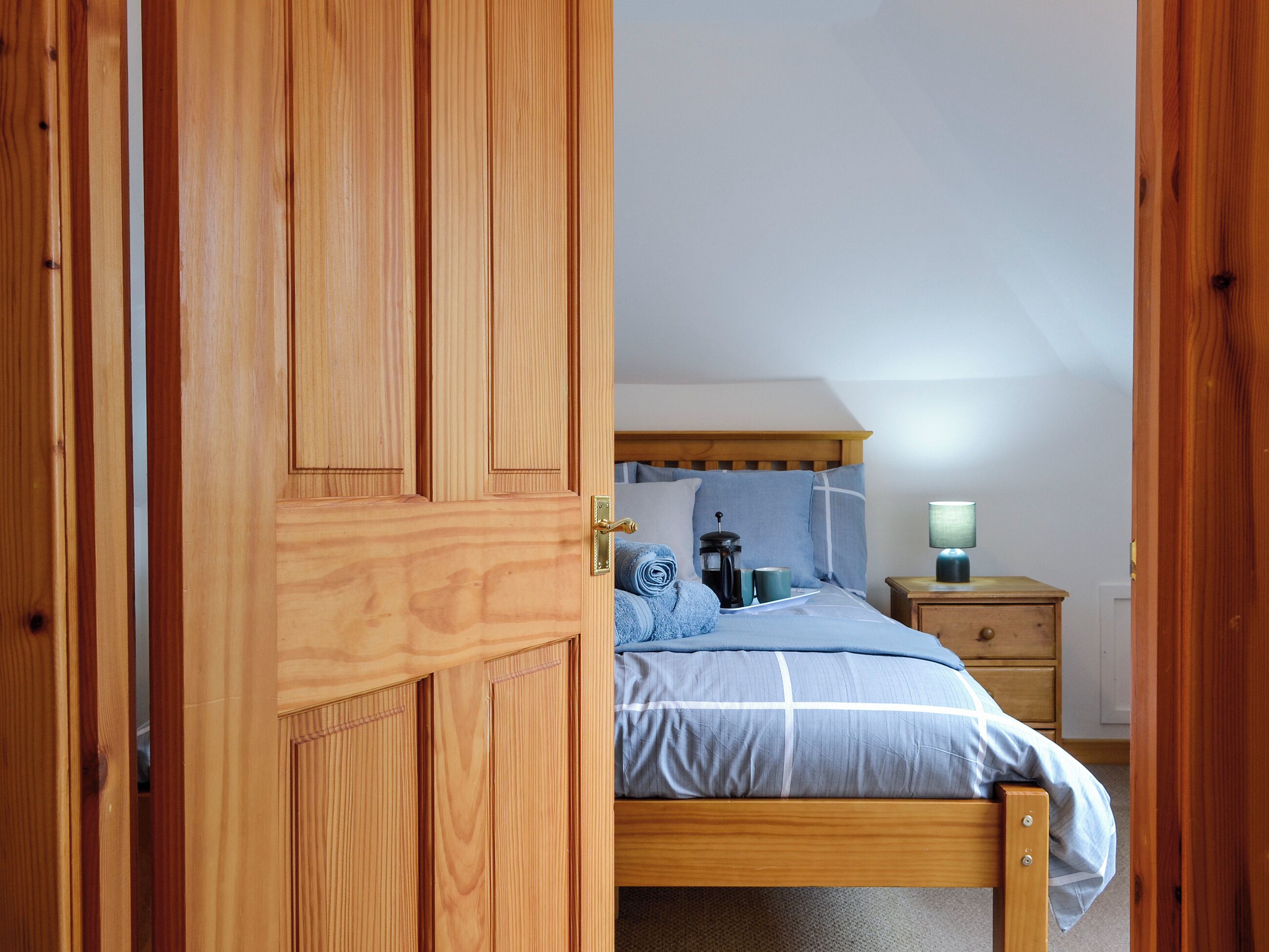 Quarto com cama de madeira, mesa de cabeceira com abajur e criado-mudo.