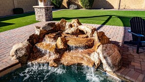 A rock waterfall feature in a landscaped area with a brick patio, a lawn, and a chair. - 6BR 5BA, Heated Pool/Spa, indoor & outdoor games, pickleball, MUCH MORE! (Glendale)