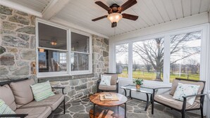 A stone-walled room with a ceiling fan, a sofa, a chair, a small table, and large windows offering a view of the outdoors. - 20 min to Sight& Sound*game room*patio*hot tub (Gordonville)
