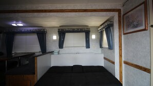 Ein kompaktes Wohnmobil-Interieur mit Bett, Küchenzeile und kleinem Fenster mit Vorhängen.