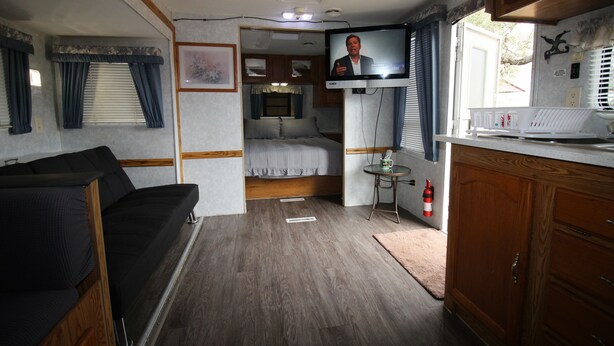 Ein kompaktes Wohnmobil-Interieur mit einer Küchenzeile, einem Bett, einer kleinen Essecke und einem Fernseher.