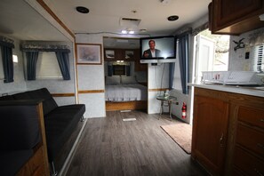 Un intérieur de camping-car compact comprenant un coin cuisine, un lit, un petit espace repas et un téléviseur.