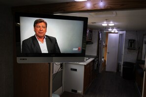 A television mounted on a wooden wall displaying a man in a suit.