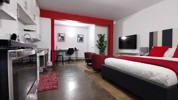 Une chambre d’hôtel moderne dotée d’une kitchenette, d’un coin repas et d’un grand lit agrémenté de touches de couleur rouge.
