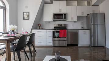 Una cocina moderna con armarios blancos, electrodomésticos de acero inoxidable y un comedor con mesa y sillas.