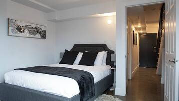 Une chambre à coucher moderne avec un grand lit, une tête de lit sombre et un mur blanc orné d’un tableau abstrait encadré.