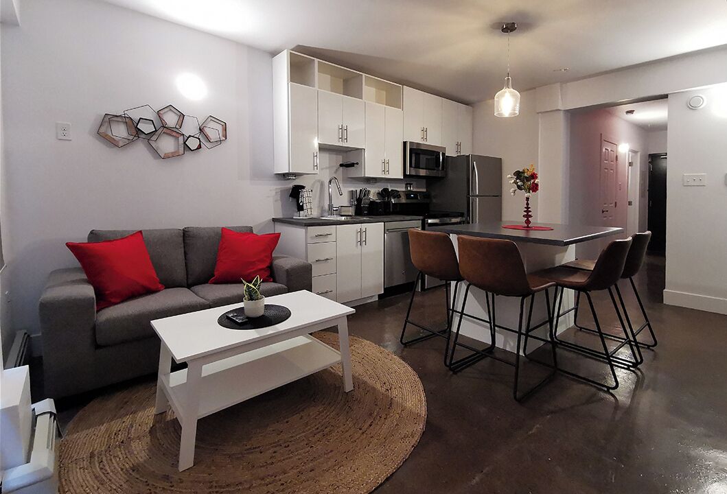 A modern kitchen with white cabinets, a microwave, and a refrigerator. There is a dining area with a table and chairs.