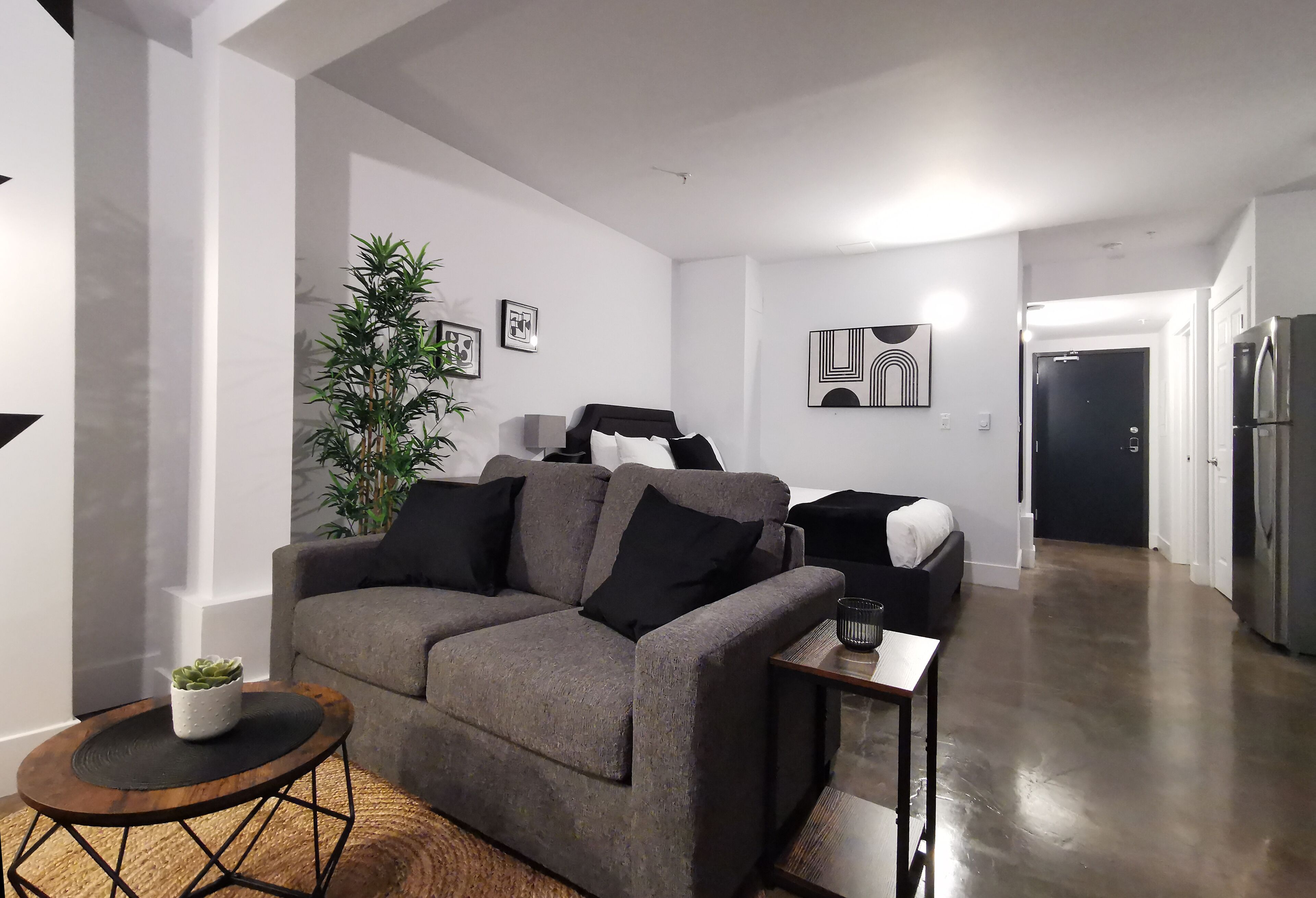 Un salon moderne avec un canapé gris, une petite table ronde en bois et une plante en pot.