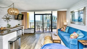 Ein modernes Wohnzimmer mit Sofa, Couchtisch, Fernseher und einem Balkon mit Blick auf die Stadt.