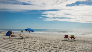Ein Strand mit Zelt, Liegen und einem blauen Sonnenschirm.