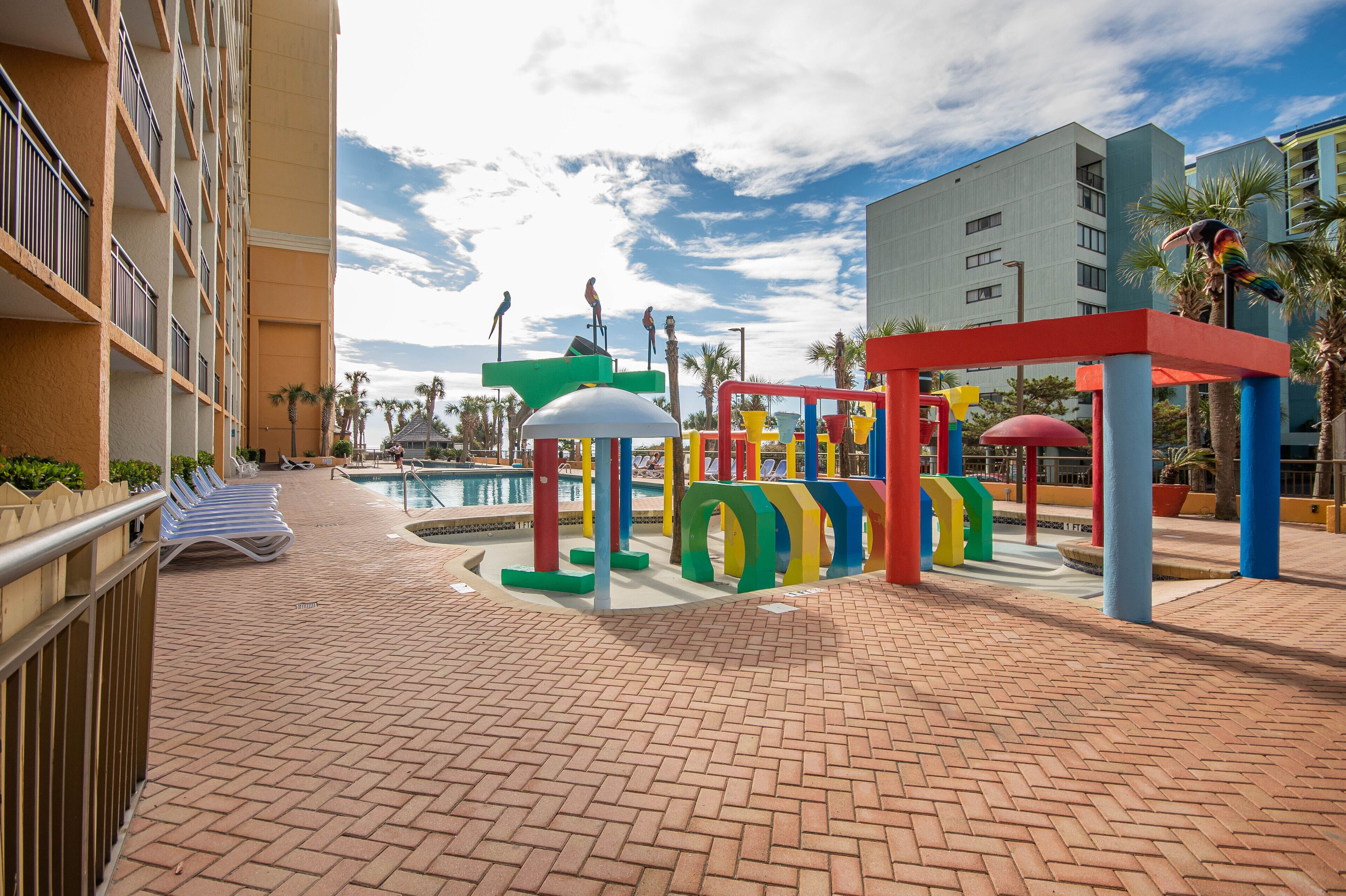 A hotel courtyard with a pool, colorful play structures, and palm trees.