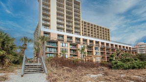 Ein mehrstöckiges Hotel mit Balkonen, Blick auf den Strand und einer Treppe zum Eingang.