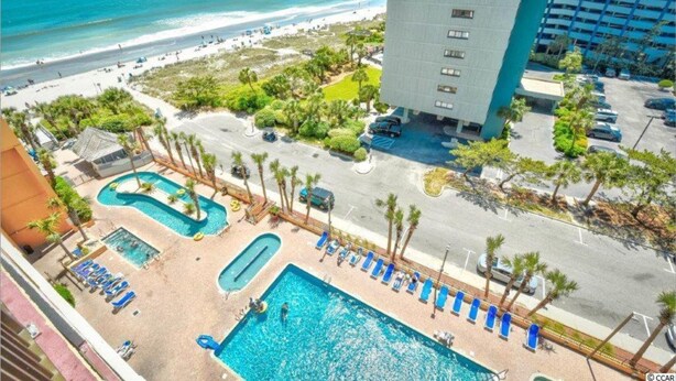 Ein Hotel mit Poolbereich, Blick auf den Strand und einem Parkplatz.
