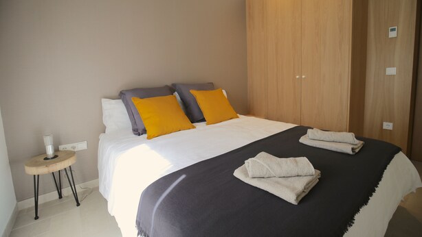 Een moderne hotelkamer met een groot bed, een houten garderobe en een klein nachtkastje met een lamp.