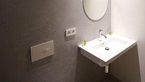 Een moderne badkamer met een witte wasbak, een ronde spiegel en een lichtschakelaar aan de muur.