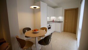 Een moderne keuken met witte kastjes, een houten deur en een eethoek met een ronde tafel en stoelen.