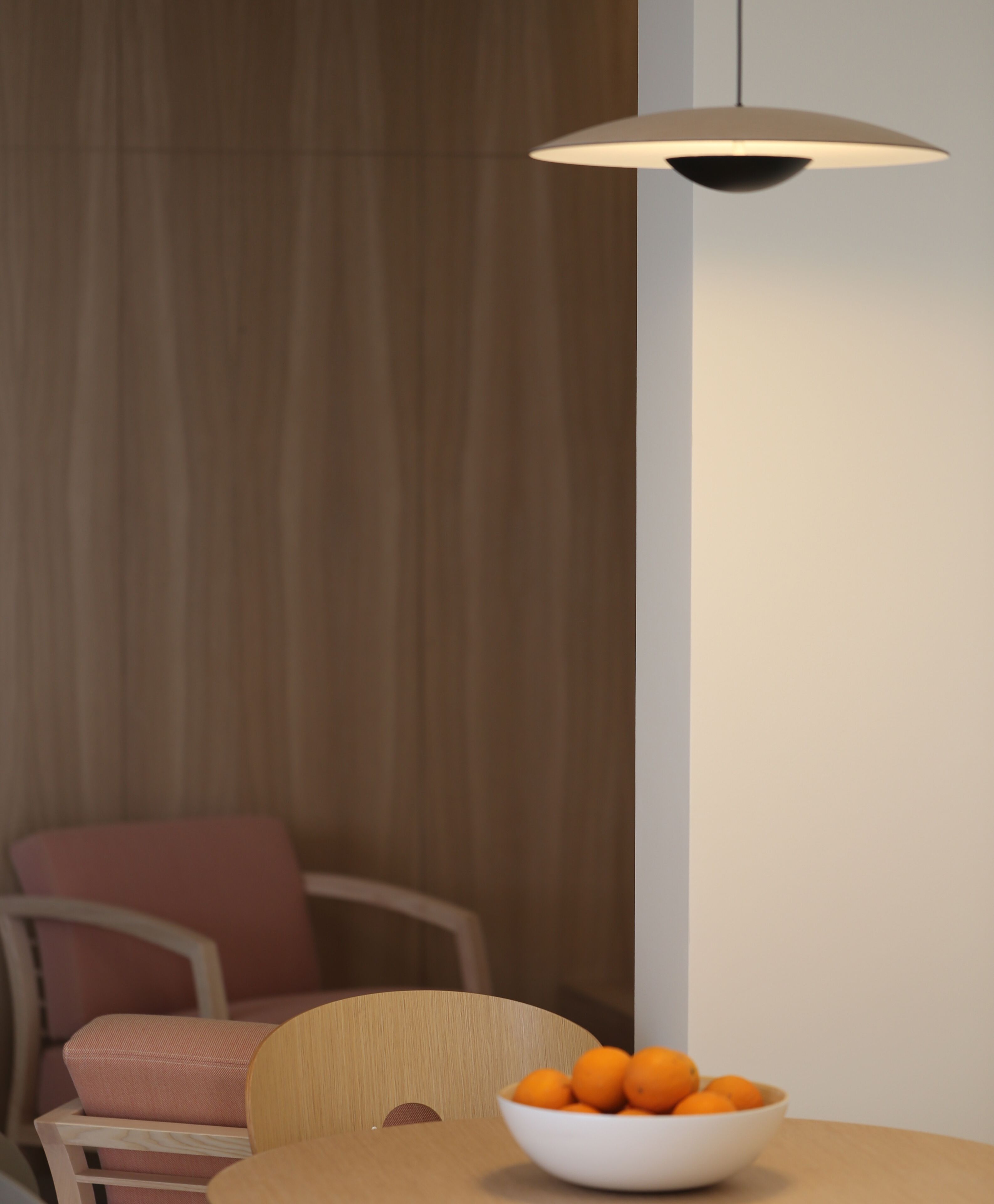Un coin repas avec une table, un saladier rempli d’oranges, une chaise et une suspension.