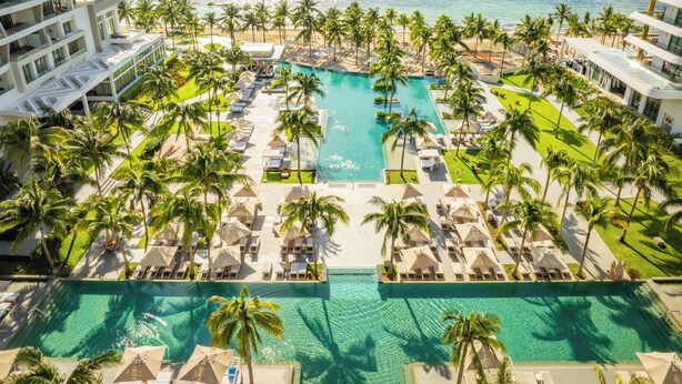 Ein Resort mit einem zentral gelegenen Schwimmbad, Palmen und Blick auf den Ozean.