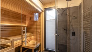 Un sauna moderne avec des bancs en bois et un espace douche clos par des parois de verre.