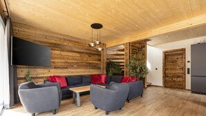 Un salon moderne avec un plafond en bois, des canapés gris, une table basse et un téléviseur fixé au mur.
