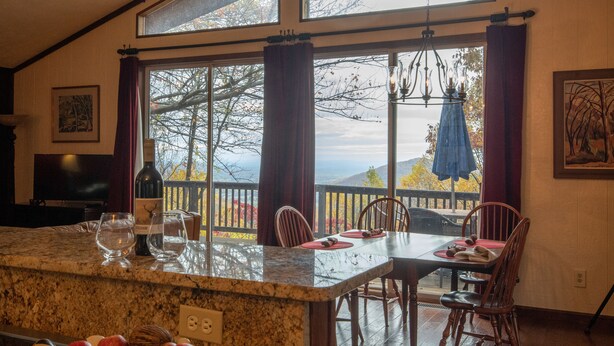 A kitchen with a large island, dining table, and chairs. There is a view of trees and mountains through large windows. - Mountain cabin by Shenandoah National Park (Stanardsville)