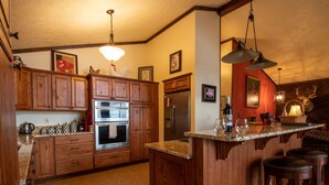 A kitchen with wooden cabinets, a stainless steel refrigerator, an oven, and a bar area with stools. - Mountain cabin by Shenandoah National Park (Stanardsville)
