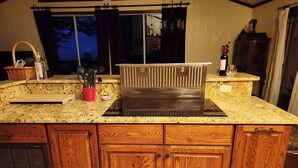 A kitchen with granite countertops, wooden cabinets, a stainless steel range hood, and a window with dark curtains. - Mountain cabin by Shenandoah National Park (Stanardsville)