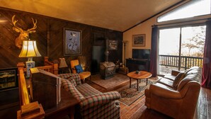 A cozy living room with a fireplace, wooden furniture, and a large window. - Mountain cabin by Shenandoah National Park (Stanardsville)