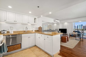 Enjoy a city view from the balcony, relax in the living area with a large flat-screen TV, and cook in the kitchen with white cabinetry.