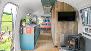 A compact kitchen with a sink, stove, and a flat-screen TV mounted on the wall. - Airstream, Devon Hideaways -  a shepherds hut that sleeps 2 guests  in 1 bedroom (Kenn)