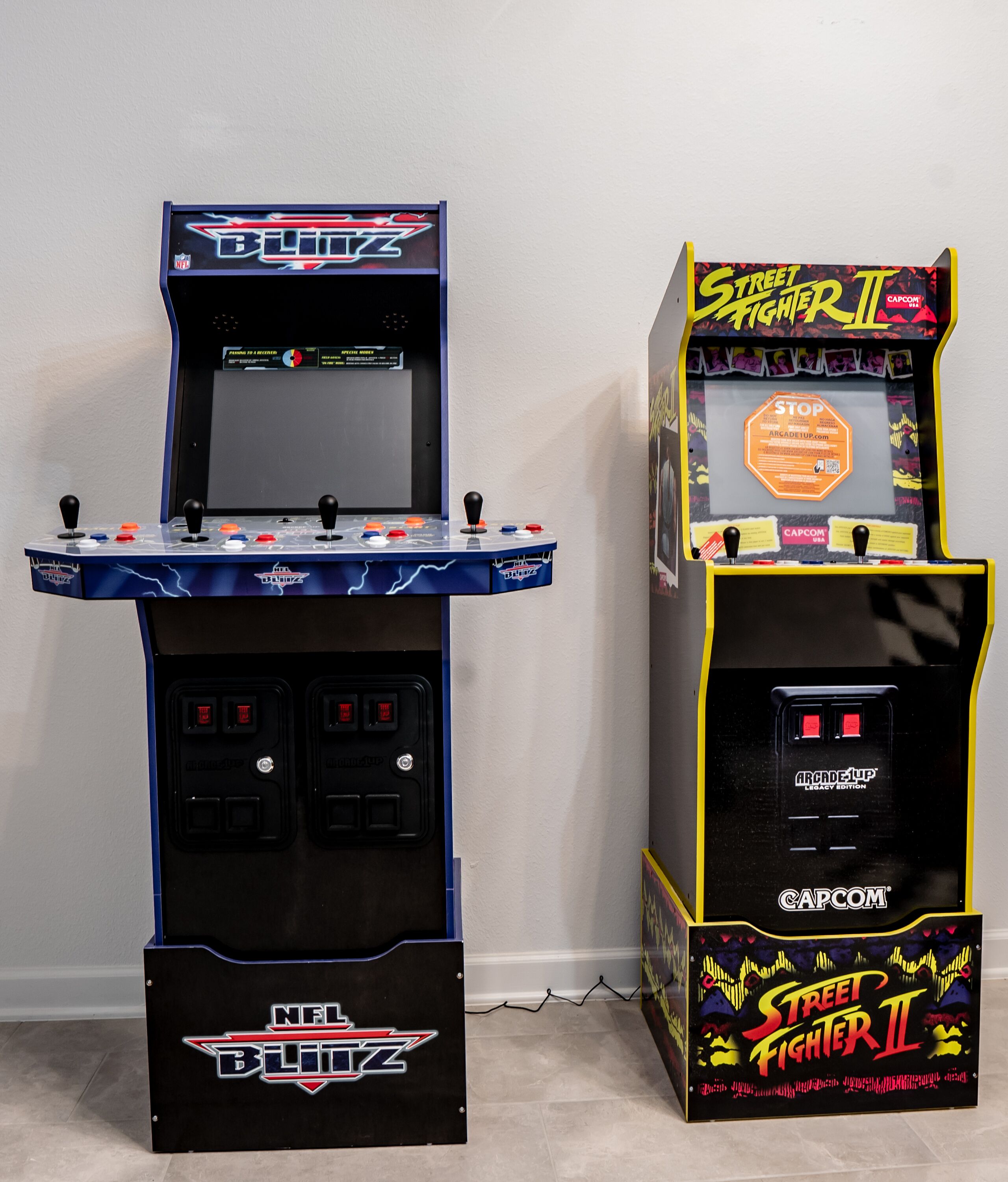 To arkademaskiner, hvoraf den ene er mærket NFL Blitz og den anden Street Fighter II, foran en ensfarvet væg.
