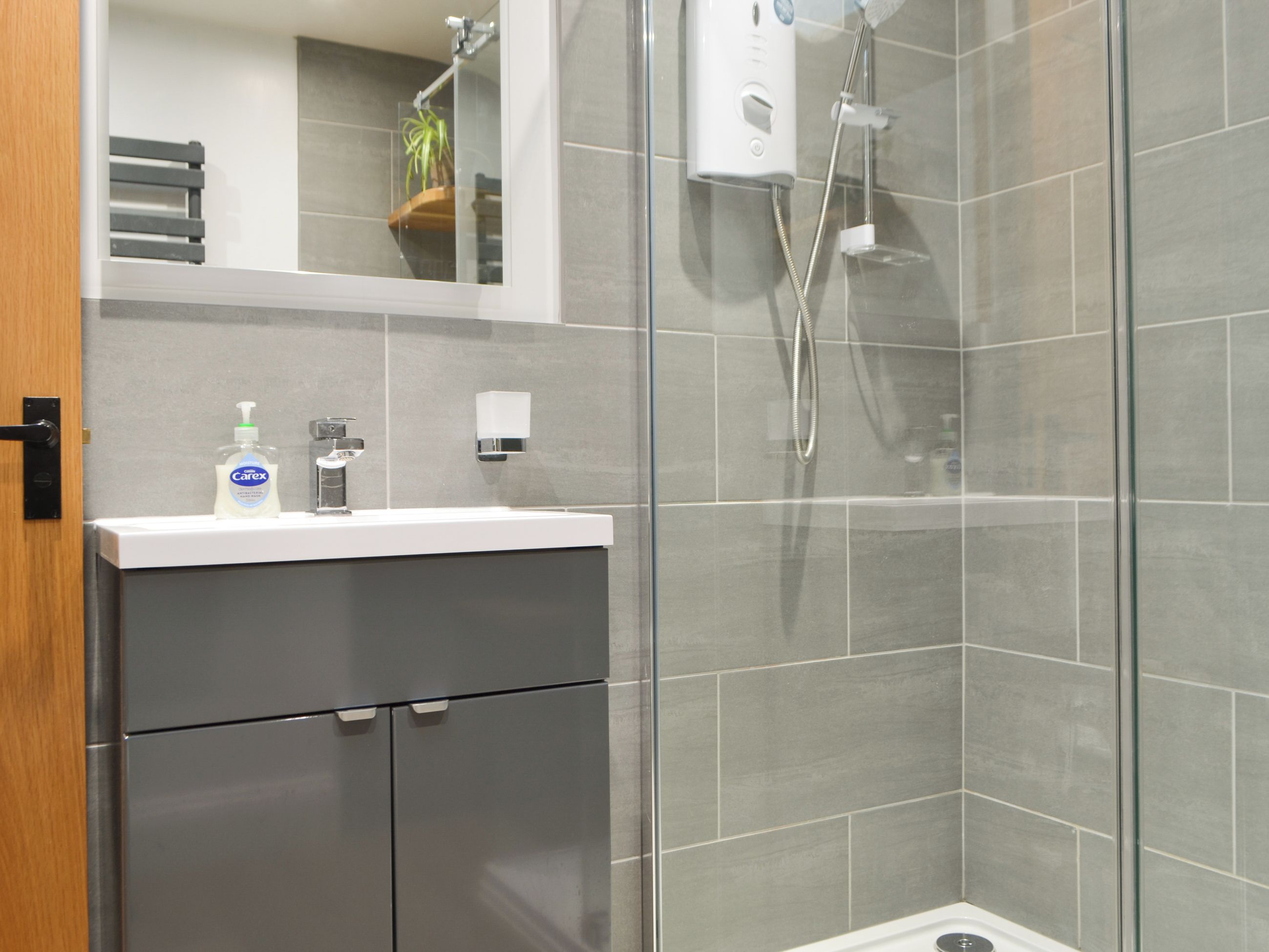 Une salle de bain moderne avec une douche à parois de verre, un lavabo blanc et un miroir au-dessus.