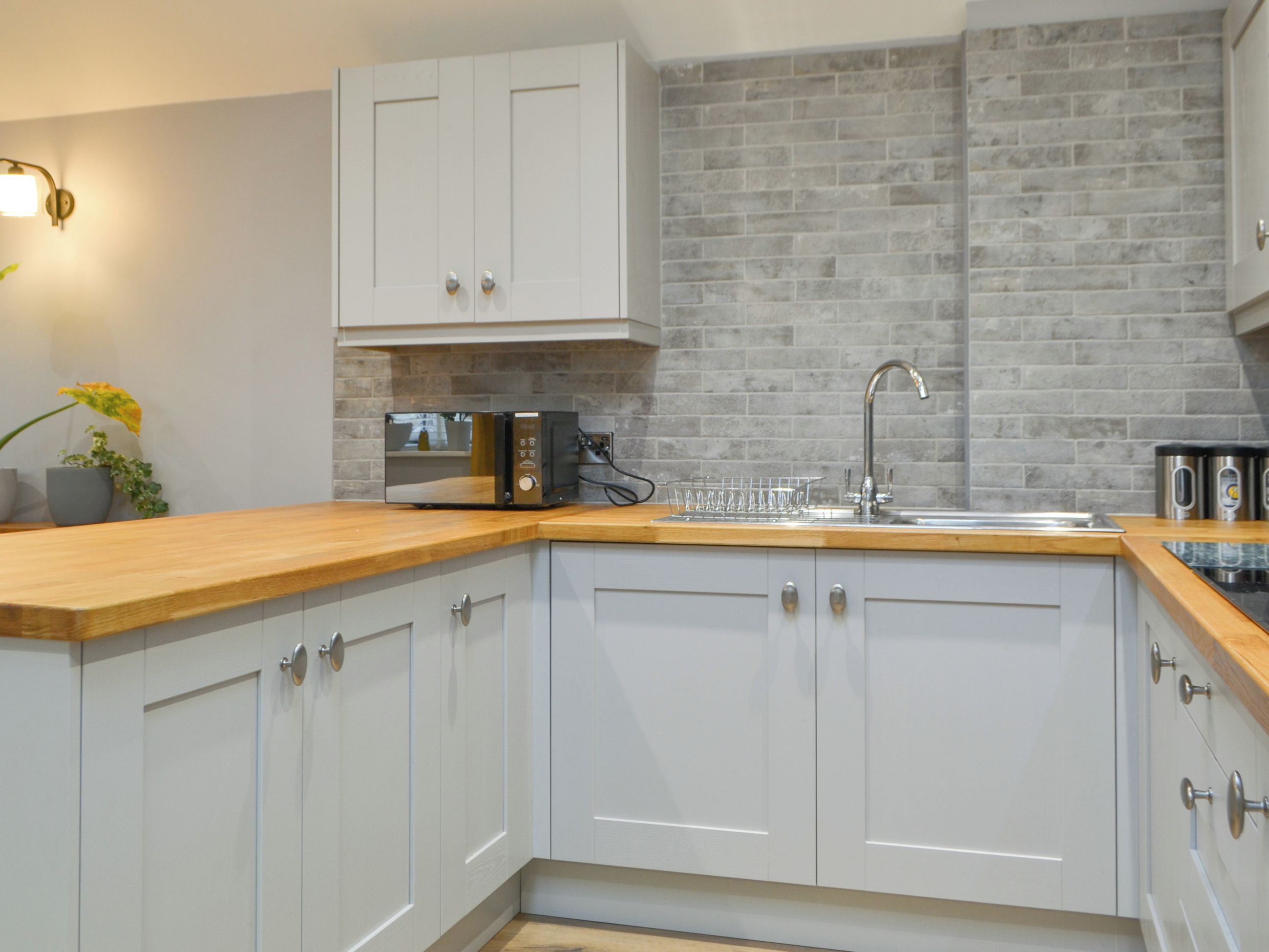 A modern kitchen with white cabinetry, a wooden countertop, a built-in microwave, and a stainless steel sink.