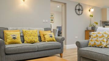 A living room with a grey sofa, yellow pillows, a wooden coffee table, and a wall-mounted clock.