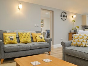 A living room with a grey sofa, yellow pillows, a wooden coffee table, and a wall-mounted clock. - 1 bedroom accommodation in Cockermouth (Cockermouth)
