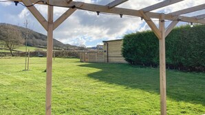 A wooden pergola structure in a grassy outdoor area with a view of a building and hills in the background. - Swallow Lodge - UK42540 (Clifford)