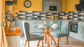 A modern kitchen with a yellow wall, a clock, and a microwave. There are two chairs with checkered upholstery and a glass table. - Swallow Lodge - UK42540 (Clifford)