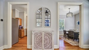 Un couloir doté d’un plancher en bois, une armoire blanche ornée de sculptures complexes, et un coin repas agrémenté d’un lustre et d’une table dressée pour quatre personnes.
